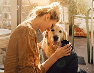 Glückliche Frau mit Hund in ihrer Wohnung mit Kaffeetasse in der Hand