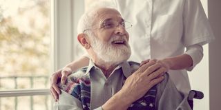 Eine Pflegerin steht hinter einem älteren Herrn, der in einem Rollstuhl sitzt