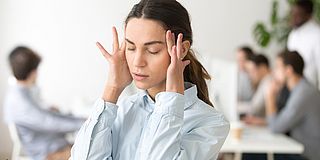 Frau reibt sich die Schläfen wegen Lärm im Büro