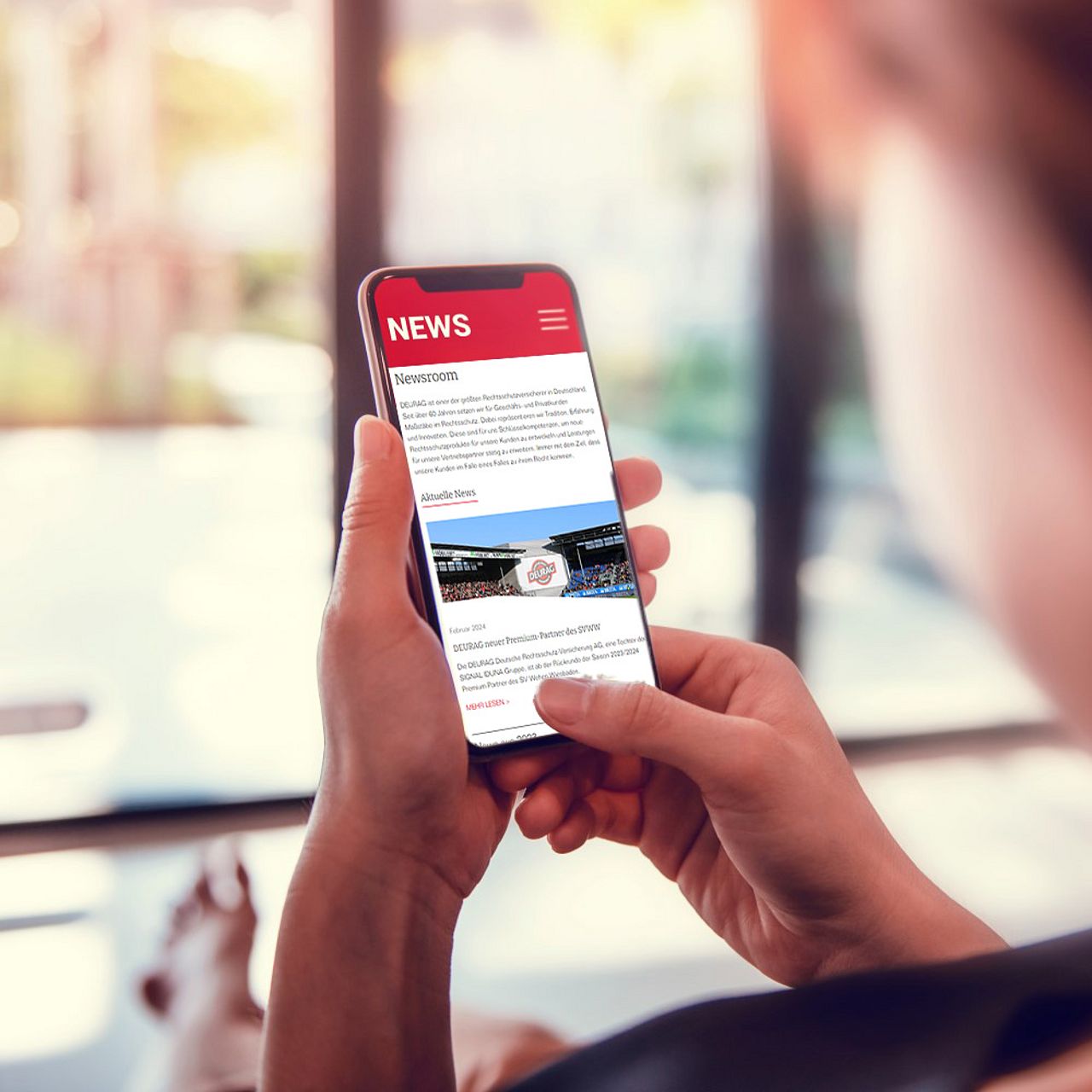 Frau hält Handy in der Hand und liest Nachrichten aus dem DEURAG Newsroom