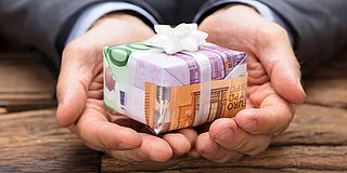 Steuerfreie Zuschüsse: zwei Hände mit Geldscheinen, die als Geschenk verpackt sind