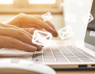 Hand eines Mannes, die eine Nachricht am Laptop sendet mit E-Mail-Symbolen