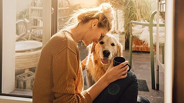 Glückliche Frau mit Hund in ihrer Wohnung mit Kaffeetasse in der Hand