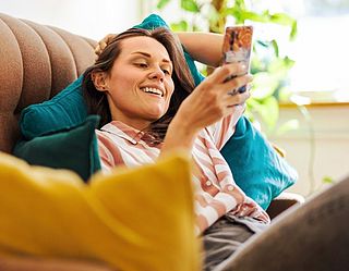Lächelnde Frau sitzt auf einem Sofa mit einem Mobiltelefon in der Hand