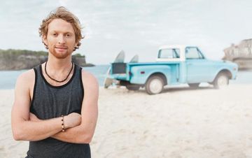 Mann steht am Strand mit Auto und Surfboard im Hintergrund