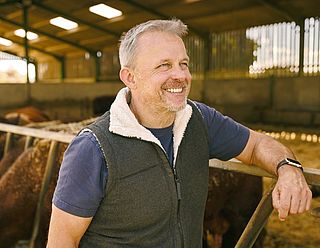 Landwirt steht draußen vor seinem Kuhstall und lächelt