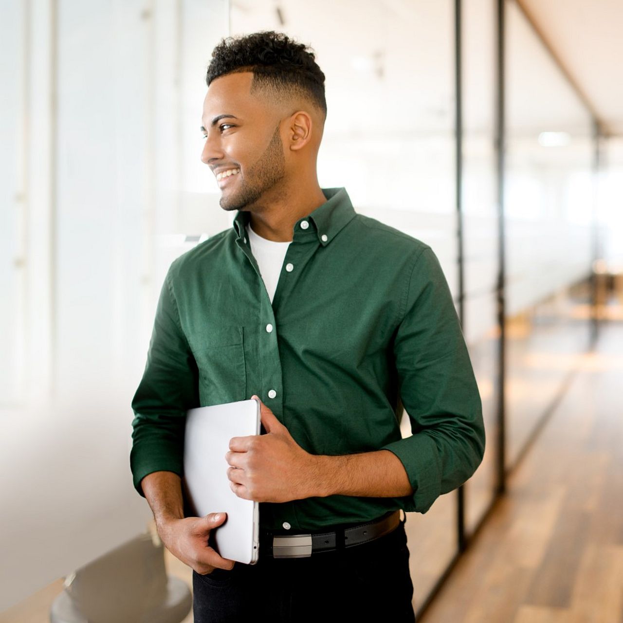 Mann steht in einem Büro und hält einen Laptop unter dem Arm