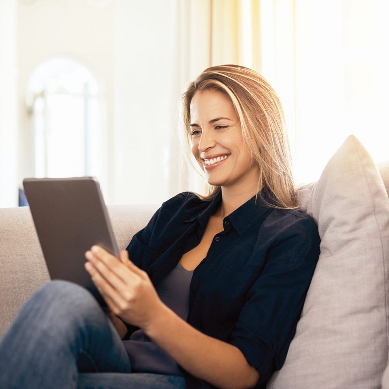 Frau bedient ein Tablet und sitzt dabei auf einer Couch
