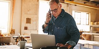 Rentner telefoniert und arbeitet am Laptop