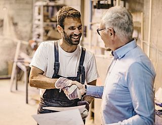 Handwerker und Kunde stehen in der Werkstatt und geben sich die Hand