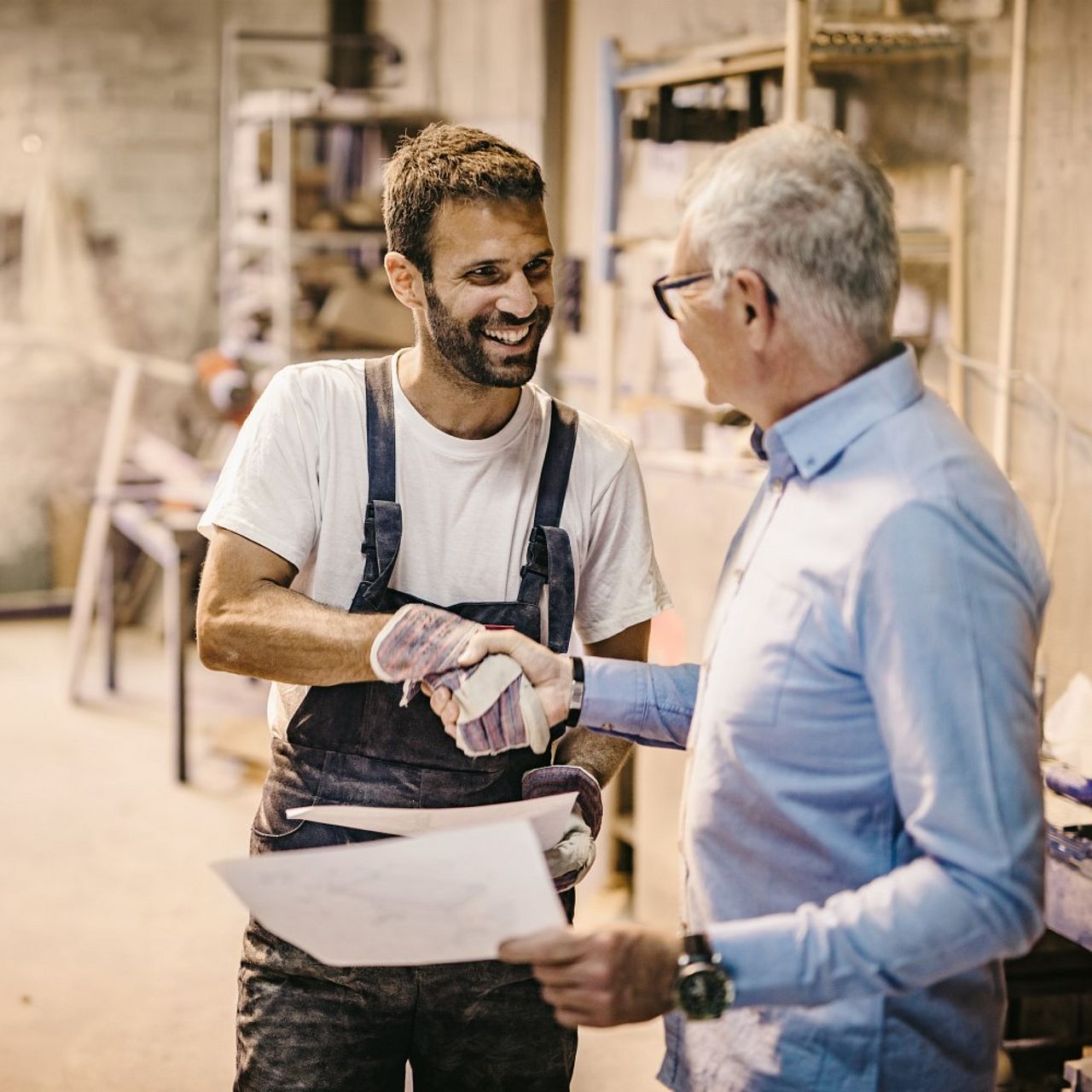 Handwerker und Kunde stehen in der Werkstatt und geben sich die Hand