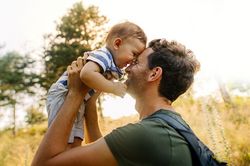 Mann hebt Kleinkind auf einem Feld hoch