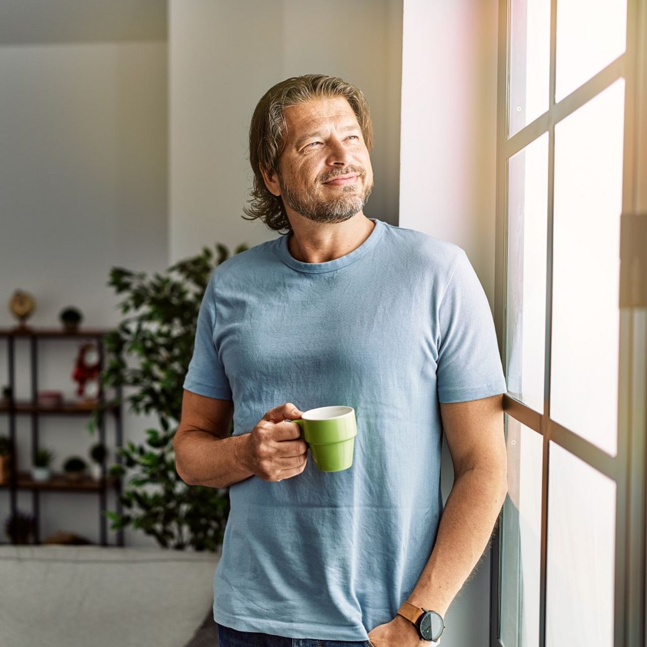 Mann hält Kaffeetasse in der Hand und schaut aus dem Fenster