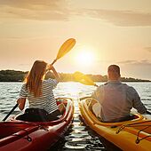 DEURAG Serviceleistungen Päarchen in Kajak paddelt Richtung Sonnenuntergang