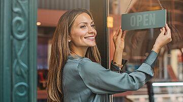 Selbstständige Unternehmerin dreht das OPEN-Schild an ihrem Laden, um den Arbeitstag zu beginnen