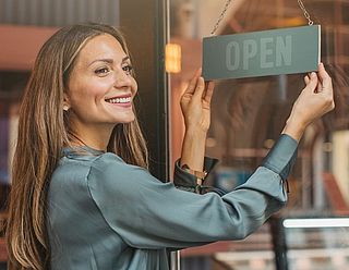 Selbstständige Unternehmerin dreht das OPEN-Schild an ihrem Laden, um den Arbeitstag zu beginnen
