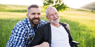 Ein Mann beugt sich hinter einem älteren Herrn, der auf einem Stuhl sitzt