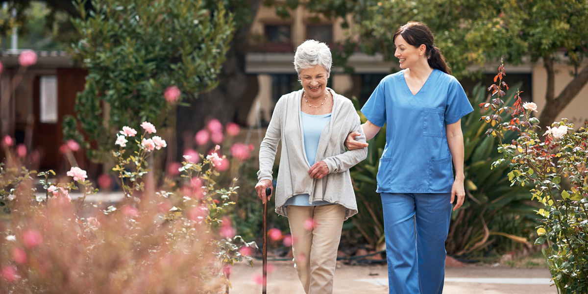 Pflegeheim-Kosten: Seniorin läuft mit Pflegerin durch den Garten