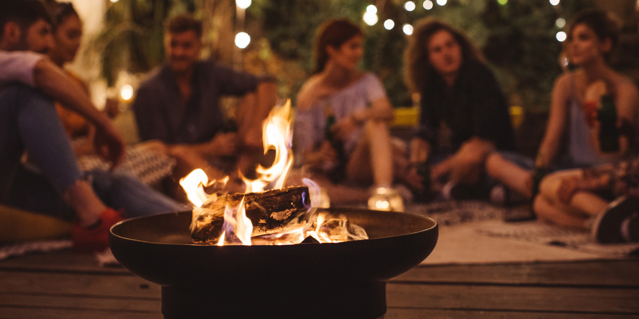 Menschen sitzen um Feuerschale im Garten